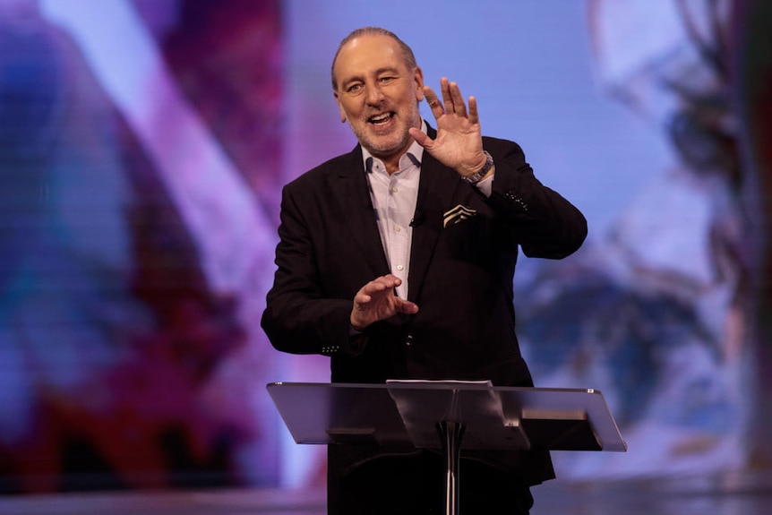 a man standing behind a lectern holding up his hand