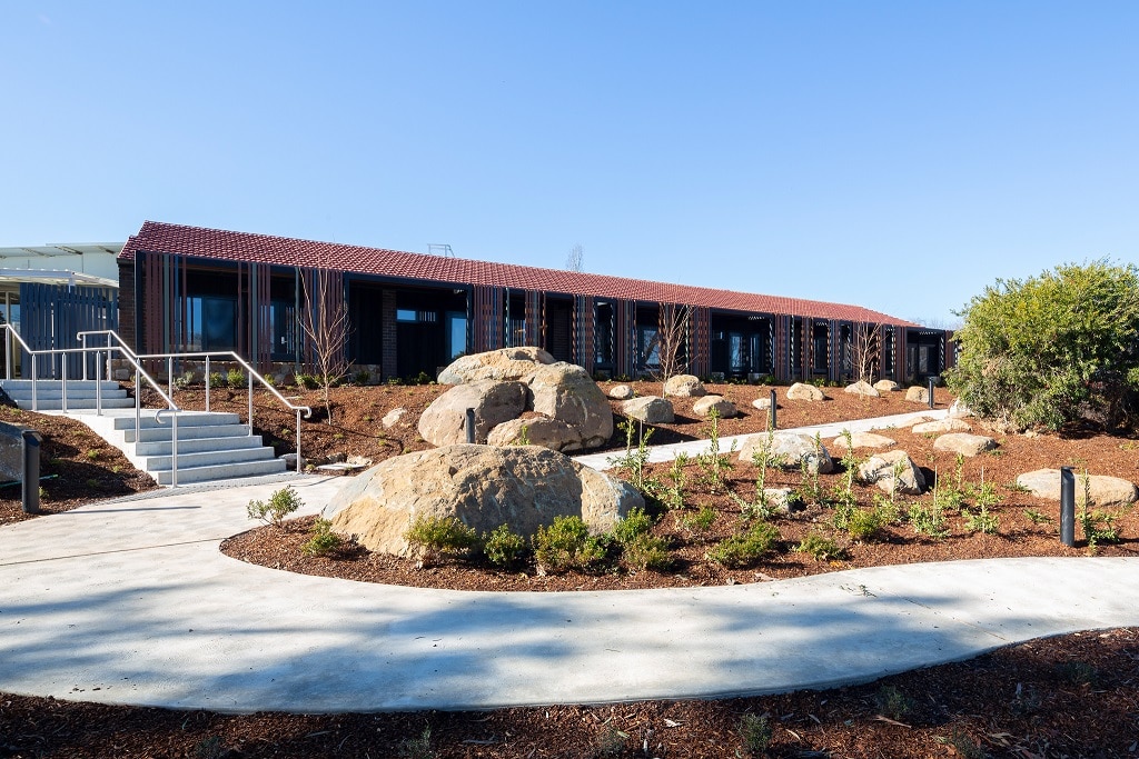The outside of a building with a winding footpath surrounding garden beds.