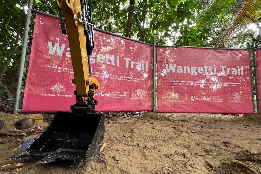 A backhoe sits idle in front of a sign at the Wangetti Trail construction site
