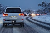 A line of cars in traffic on a snowy road.