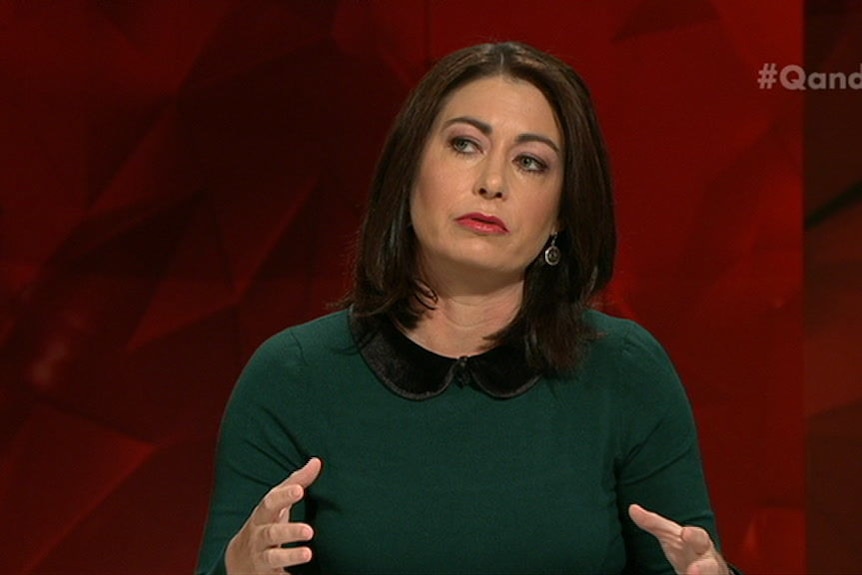 A woman with dark hair and a dark green dress speaking on a television show.