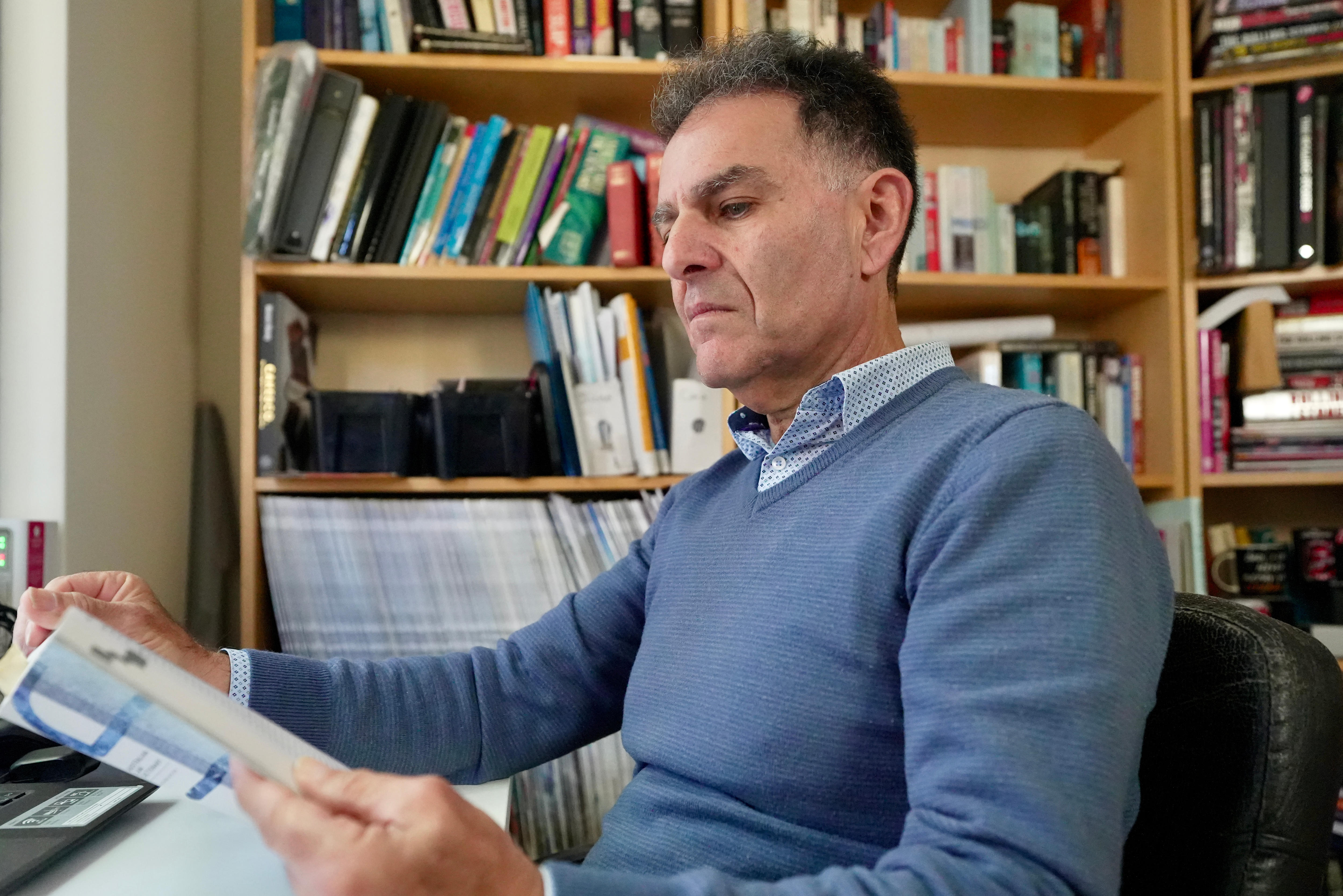 O professor sênior de direito da Curtin University, Dr. Stephen Monterosso, está sentado em sua mesa em seu escritório, lendo um livro.