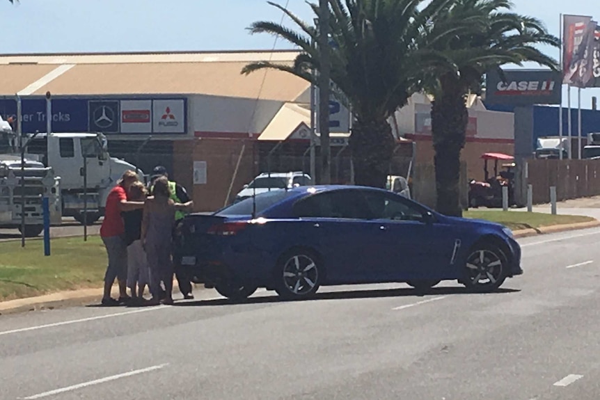 People on  the corner of Boyd Street and Flores Road in Geraldton near a blue car.