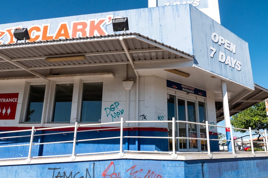 An image of an old, abandoned building with faded signage. The walls are covered in graffiti.
