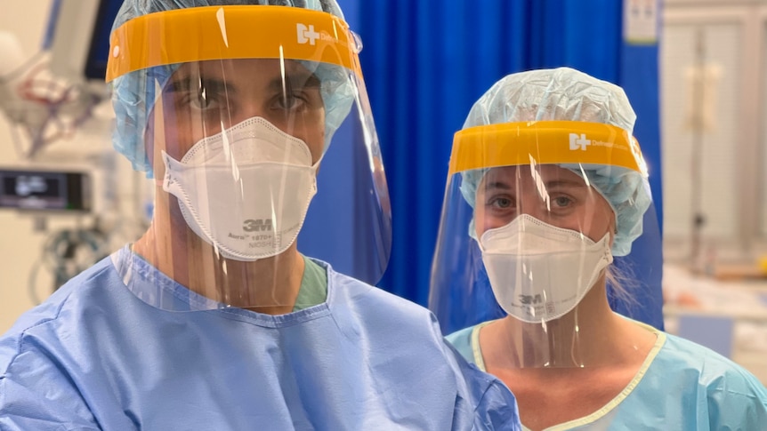 A male and female nurse standing, wearing full PPE. 