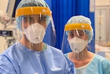 A male and female nurse standing, wearing full PPE. 