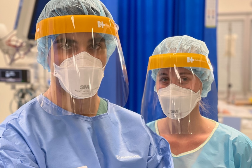 A male and female nurse standing, wearing full medical protective gear
