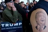 Tattoo of Donald Trump's face on a supporter's upper arm with another supporter holding a sign reading TRUMP.