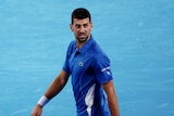 A male tennis player, holding his racquet, in all blue on a blue court, looks upset.