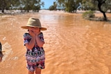 A little girl stands in front of a flooding creek.