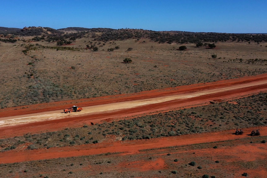 A drone shot of a road machine going along a dirt road in the outback.
