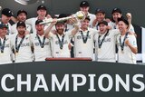New Zealand's players stand in front of a big sign that reads CHAMPIONS. Kane Williamson is holding a gold sceptre
