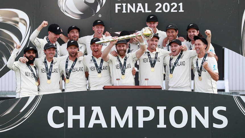 New Zealand's players stand in front of a big sign that reads CHAMPIONS. Kane Williamson is holding a gold sceptre