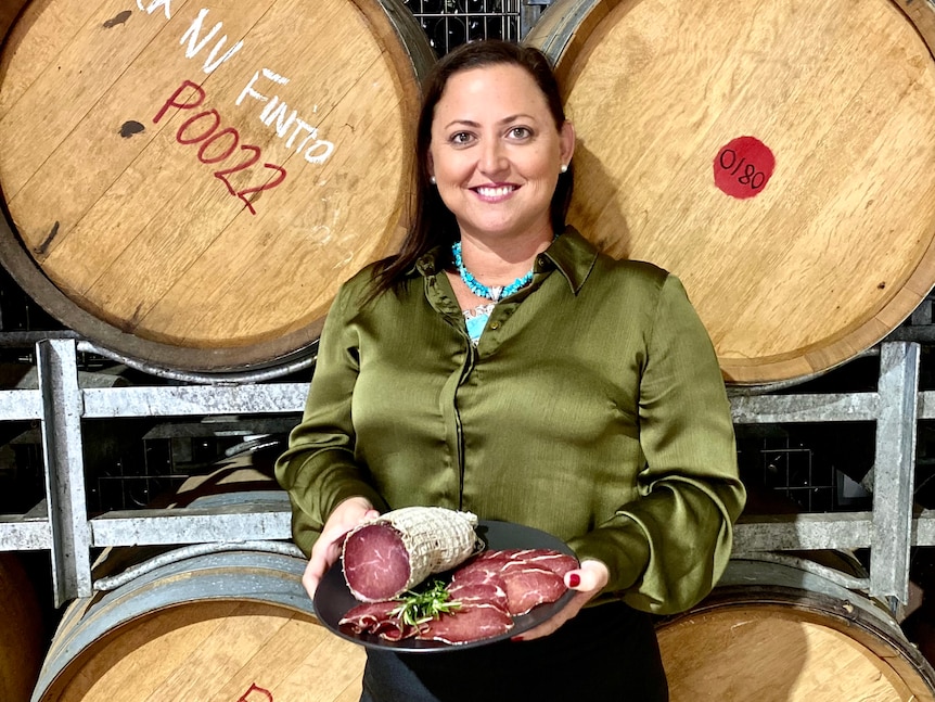 Beef producer Sonya Comiskey holds a plate of smallgoods while standing in front of two barrells.