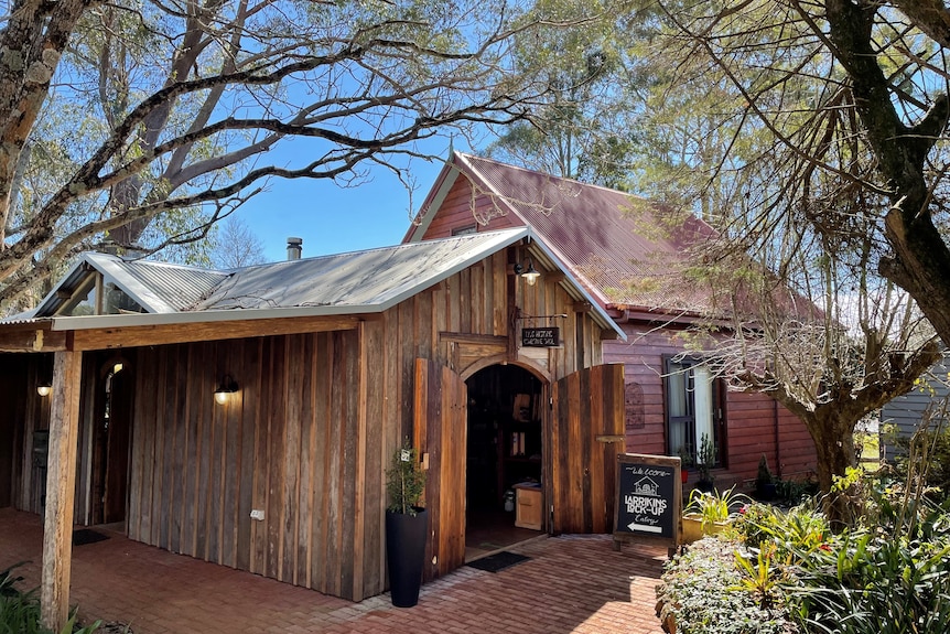 An old timber building, with a pitched roof, surrounded by large trees.