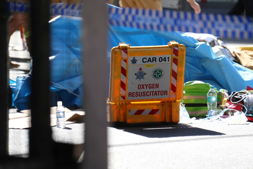 A yellow box labelled "oxygen resuscitator" amongst debris on a street.