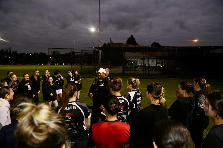 A man addresses a womens football team. 