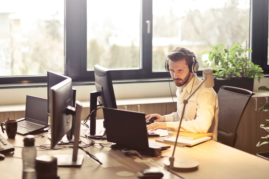 An office worker sits alone at a shared desk to represent the isolation that work addiction can cause.