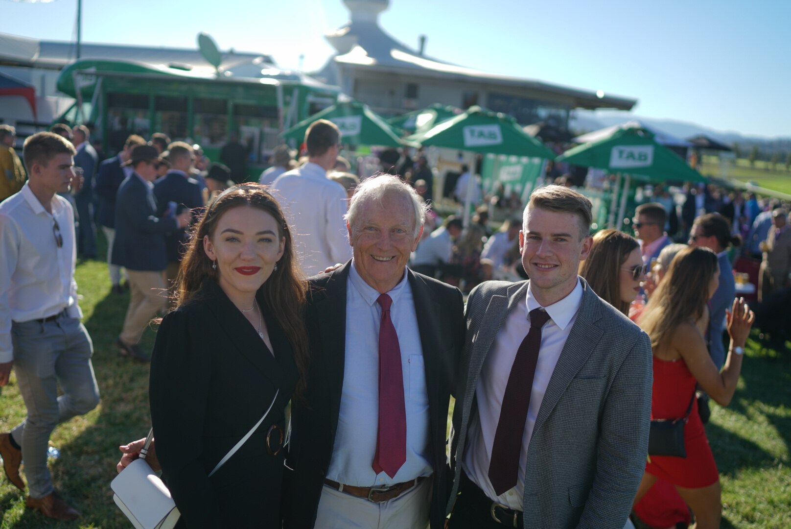 three people stand together and smile at a camera at a race club meet