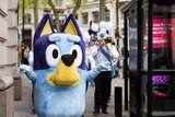 A mascot of Bluey from the TV children's show with a brass band behind it.