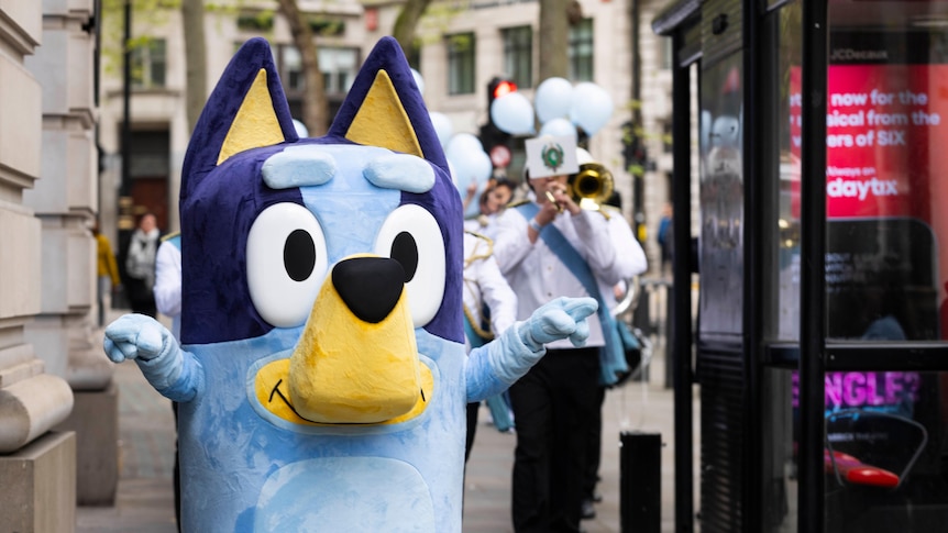 A mascot of Bluey from the TV children's show with a brass band behind it.