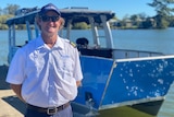 A man in a skipper's shirt standing in front of a bright blue boat