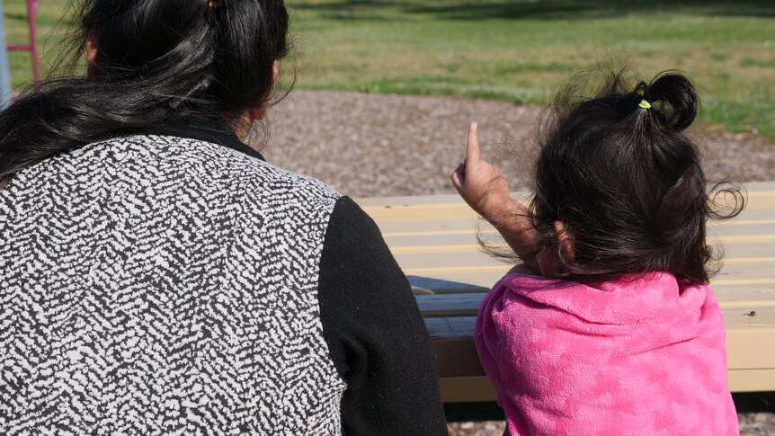 A woman and child in a park photographed from behind. 