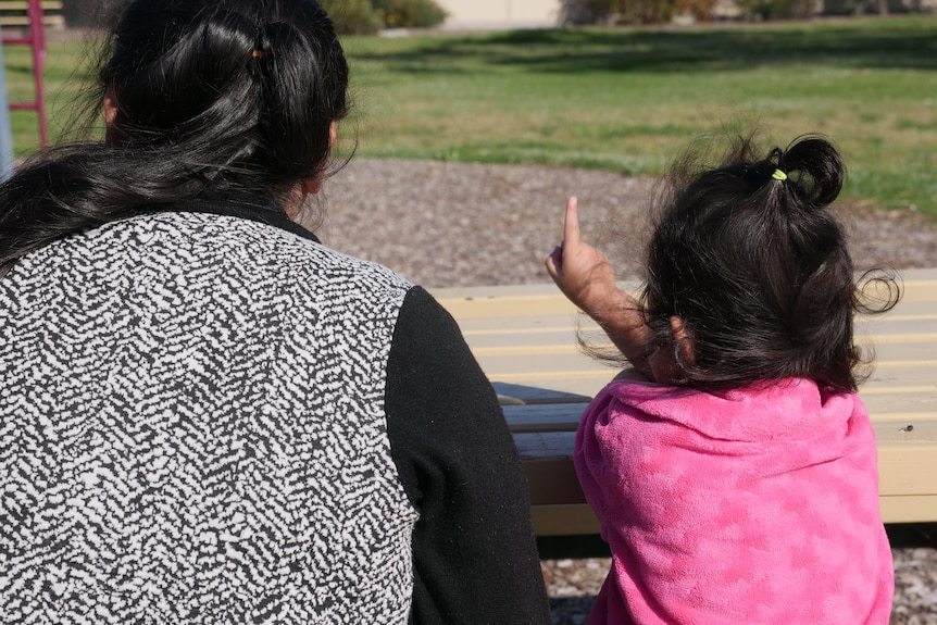 A woman and child in a park photographed from behind. 