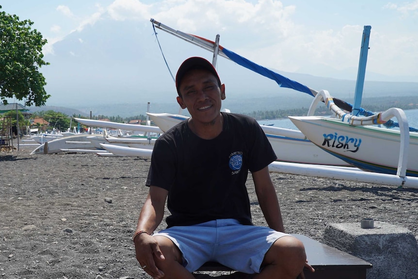 Restaurant worker Komang Putra sits on the beach with boats.