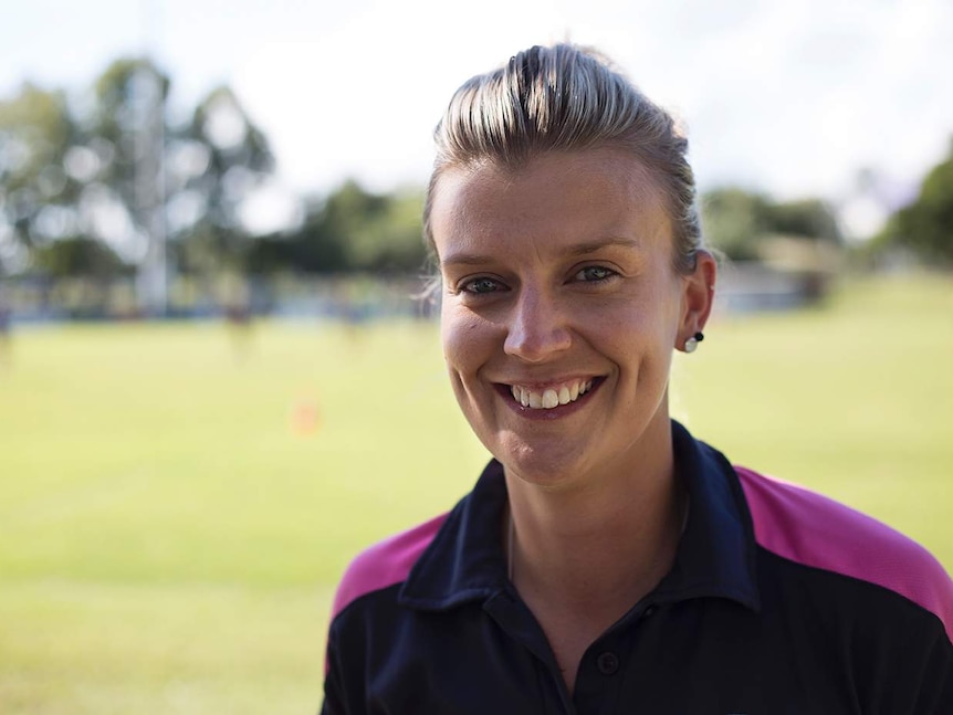 A woman looks at the camera smiling, rugby league field in the background.