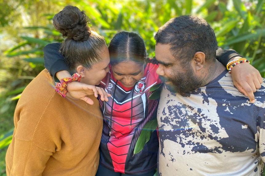 Teen Aboriginal woman with her parents, hugging tight and all looking together smiling