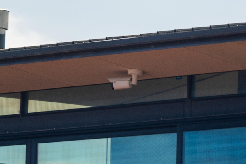 A camera affixed to the underside of a roof in a coastal area, under cloudy skies.