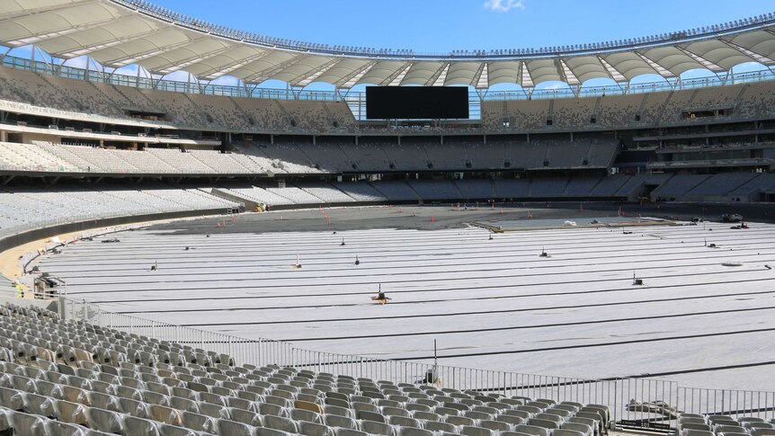 A wide shot of the interior of Perth Stadium with rows of white seats filling the stands and a wide screen at the end.