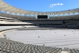 A wide shot of the interior of Perth Stadium with rows of white seats filling the stands and a wide screen at the end.