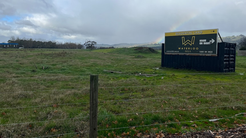 paddock with fence in the foreground and a sign advertising waterloo development in the background