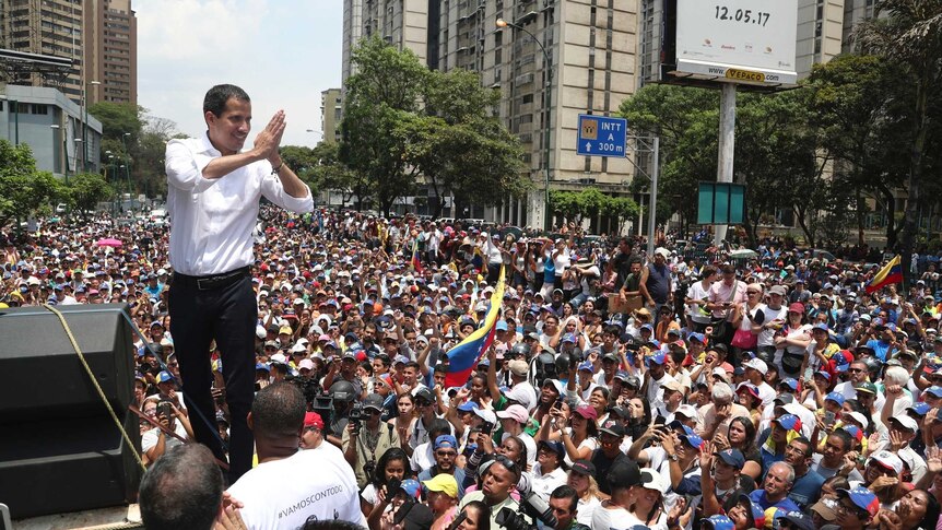 Opposition Leader Juan Guaido presses his hands together in thanks and gestures to a crowd of hundreds of people.