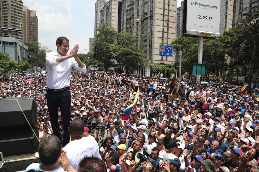 Opposition Leader Juan Guaido presses his hands together in thanks and gestures to a crowd of hundreds of people.