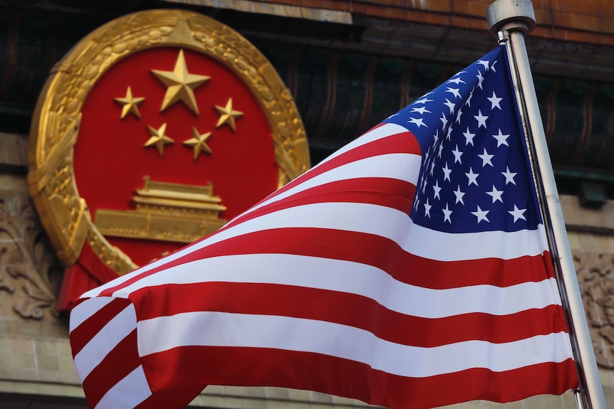 The US flag is waving in front of the red and gold round symbol of China.