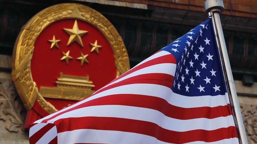 The US flag is waving in front of the red and gold round symbol of China.