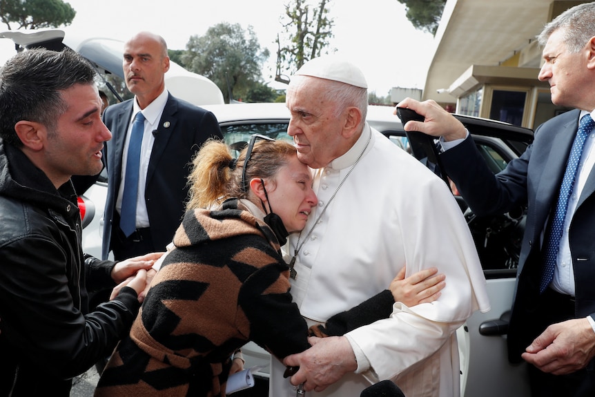 A crying woman hugs Pope Francis as he stands beside a car.