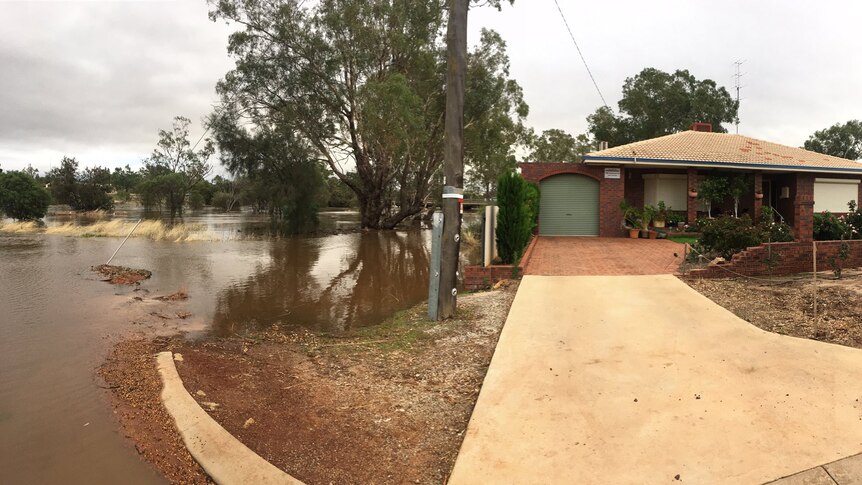 Brown water from an overflowing river creeps up towards the side of a house and a road.