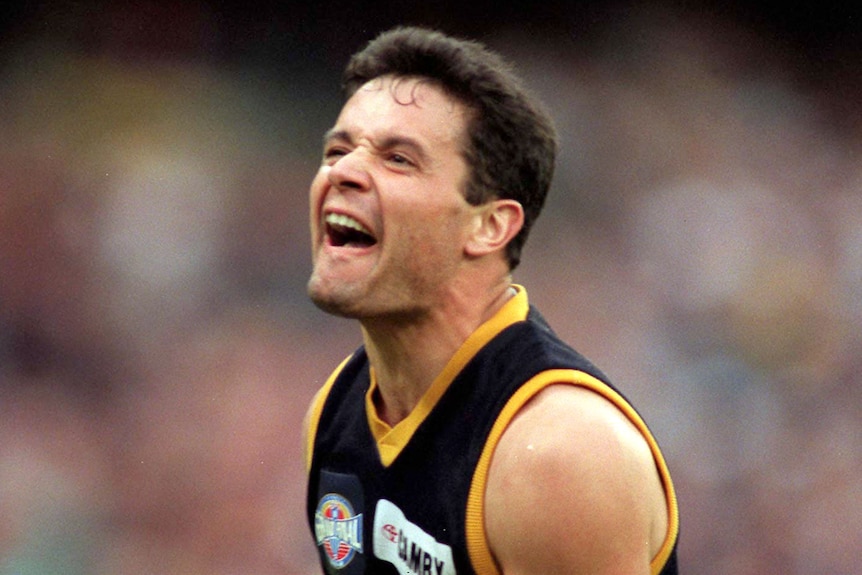 A footballer screams in a joy while wearing a yellow, red and blue jumper.