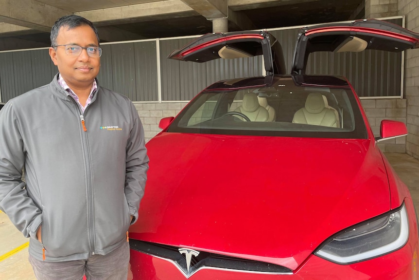 A man standing in front of a red electric car. 