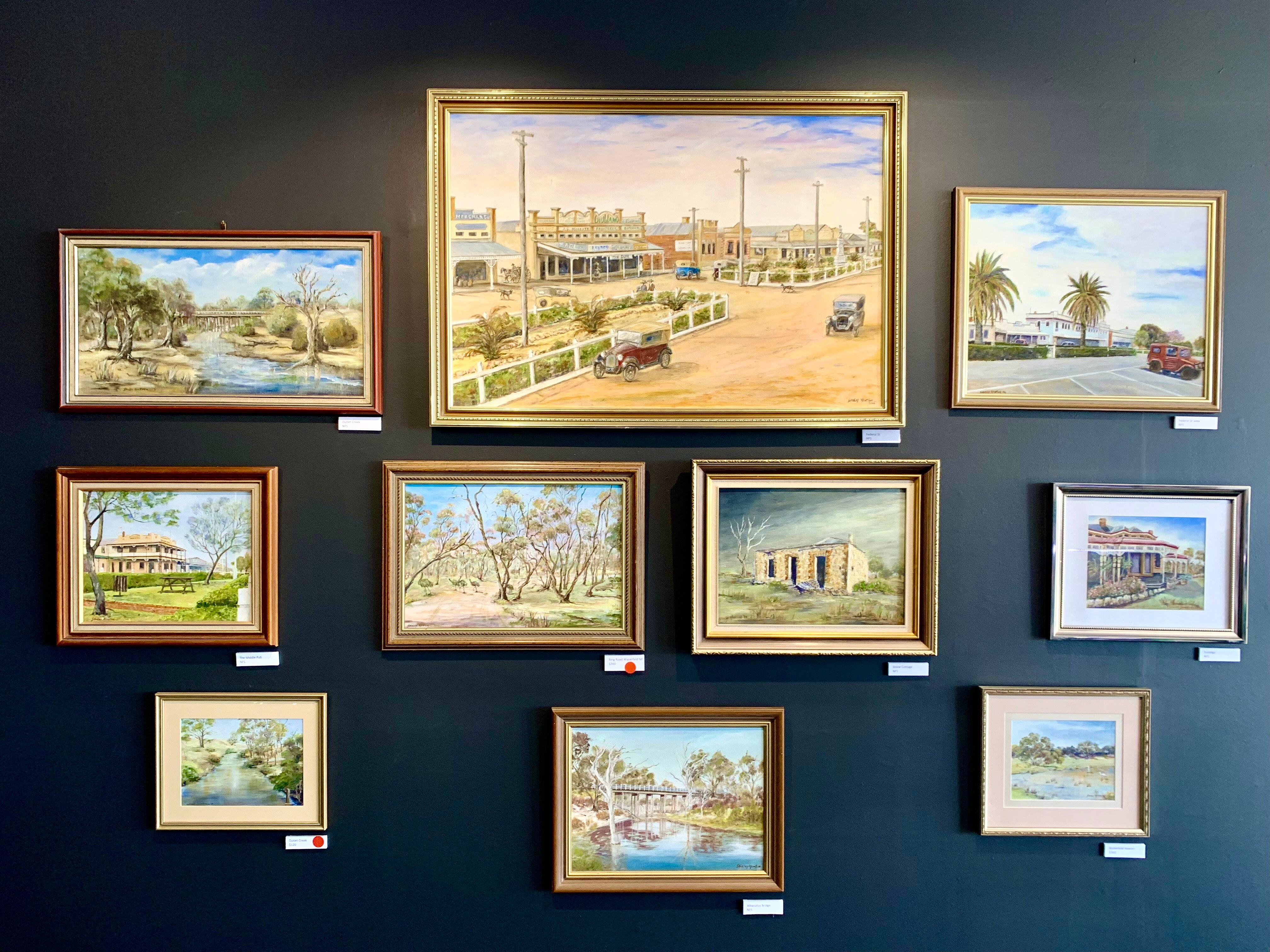 Various small paintings on a grey wall in a gallery 