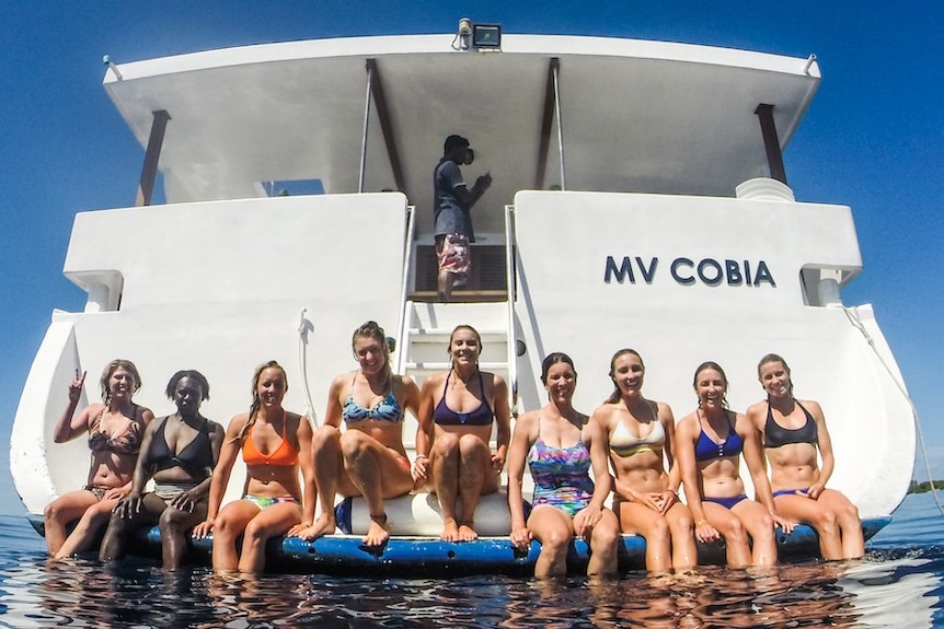 Women in swimwear on the back of a boat on the water, smiling