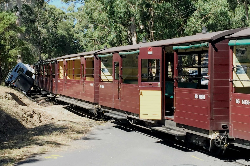 The Puffing Billy train sits stopped on the tracks next to a minibus.