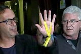 Survivors hold up a yellow ribbon as they speak to the media.