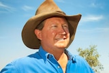 Andrew Forrest wears a hat and blue shirt and is standing in front of cattle.