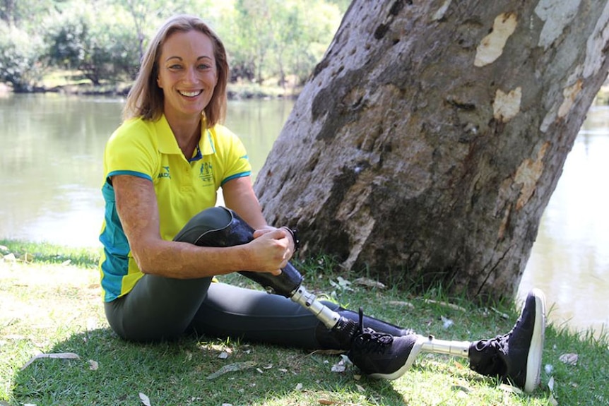 A women in a yellow shirt sits on a riverbank, para-athlete with prosthetic legs