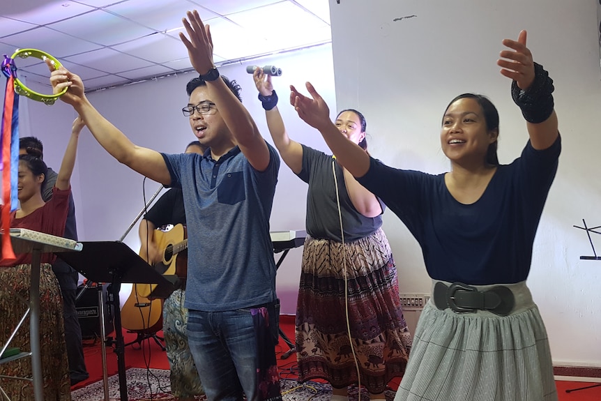 Four people stand on a stage holding their hands up in the air.